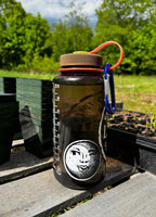 Clear tinted water bottle with a black and white circular sticker with an illustration of a feminine face peeking out behind a crescent moon on a wooden surface outdoors.