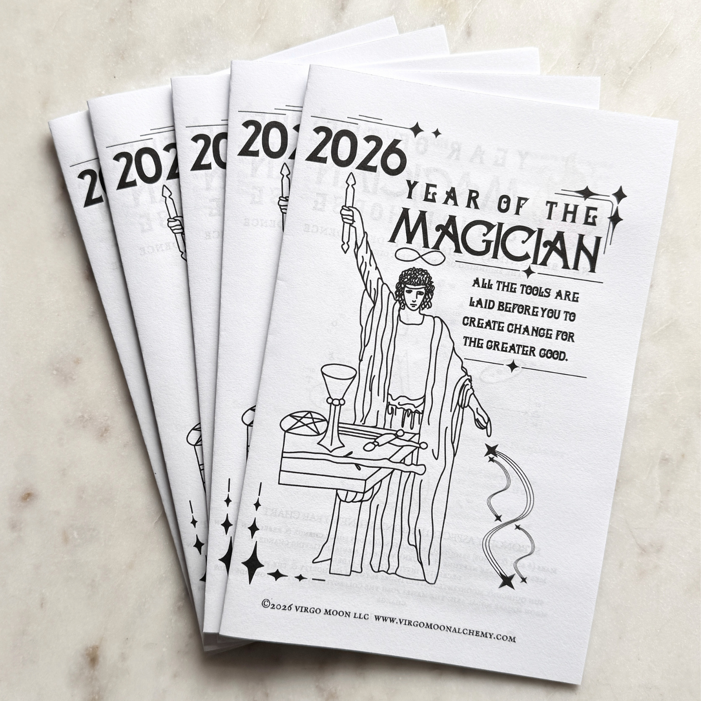 Set of printed copies of the Year of the Magician 2026 astrology guides by Jilly Andromeda on a marble surface